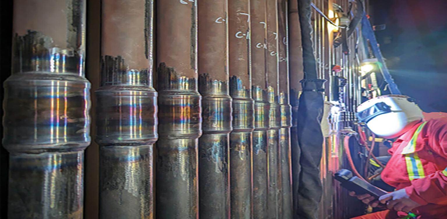 Row of installed TTPS sleeve connections with an operator and welding equipment on the right
